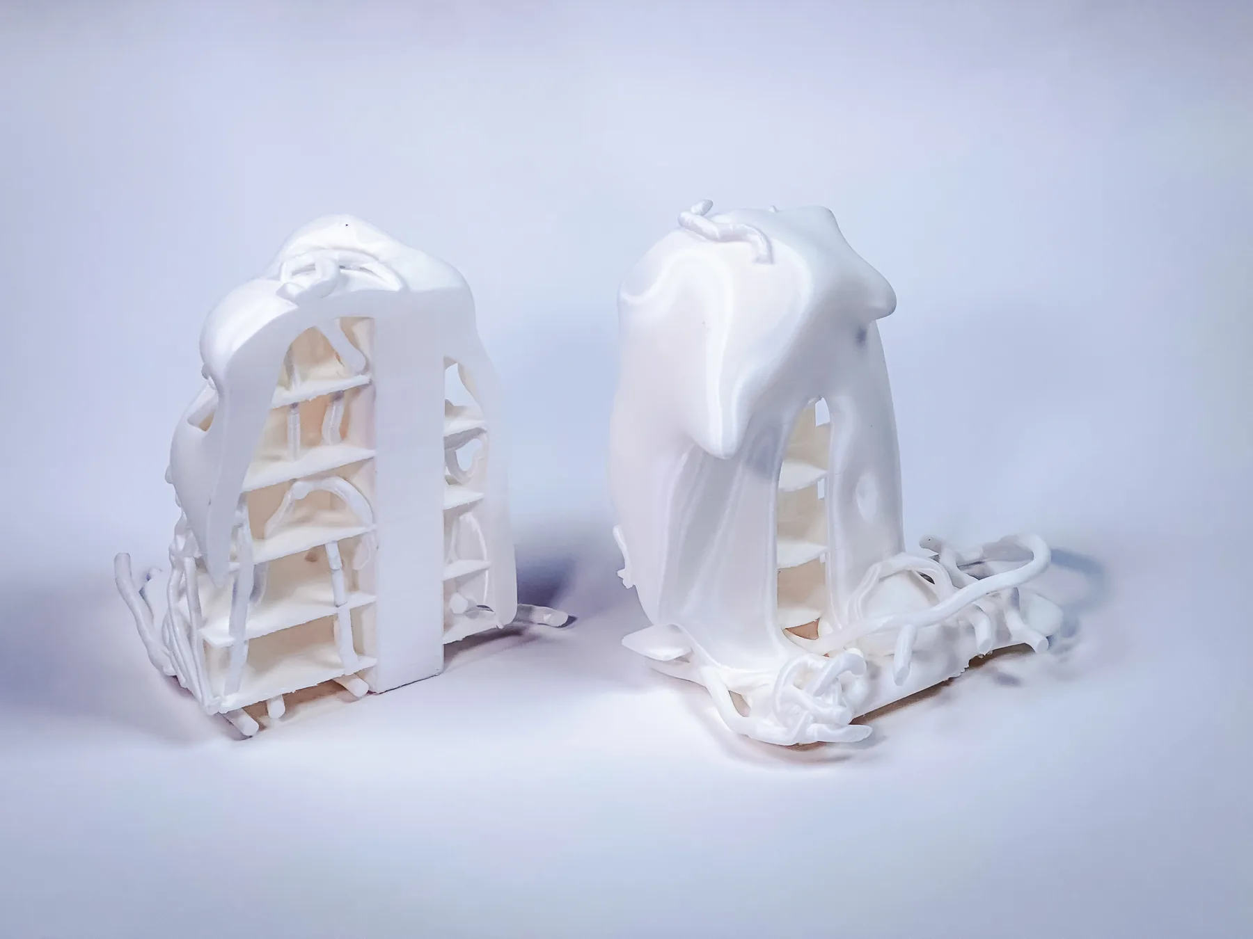 Two white 3D-printed physical study models of paired gate-like forms, photographed against a blue-white background.